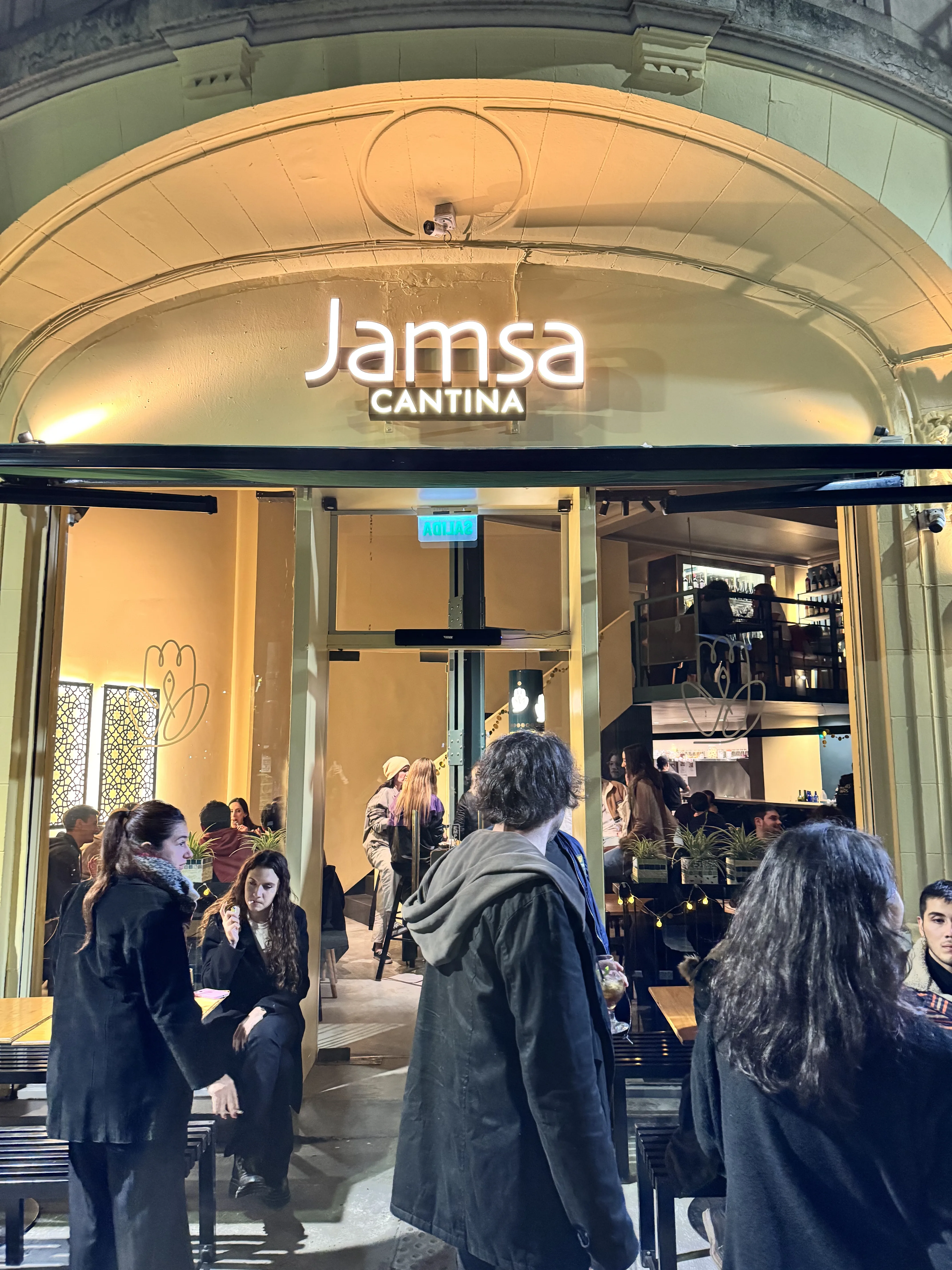 Entrada de Jamsa Cantina de noche, con el cartel iluminado sobre el toldo y el comedor a la vista